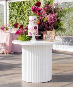 White ripple round display table with a ribbed pedestal base, styled for cakes, floral arrangements, signage, and elegant event décor.