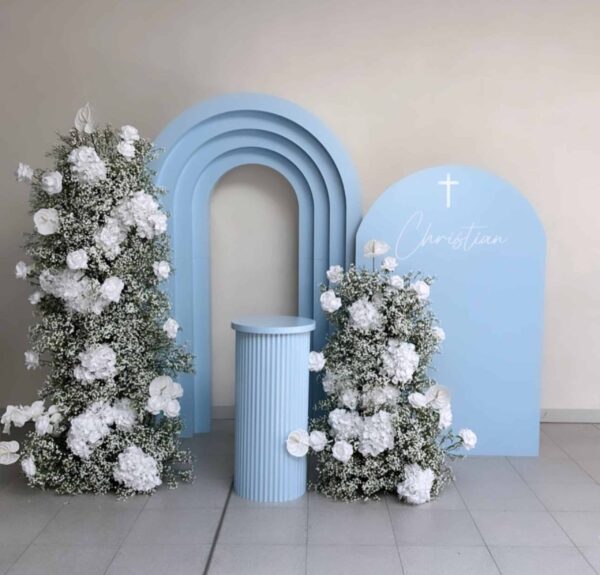 Light blue bliss baby package for baptism backdrop setup with floral columns and white baby’s breath arrangements.