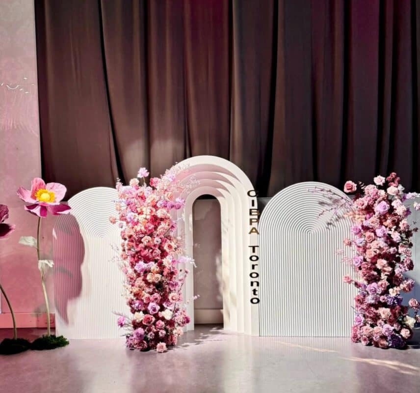 Elegant corporate event décor rental at Liberty Grand Toronto featuring white ripple backdrops, floral arches in blush and mauve, and modern backdrop design for the Women in Leadership Gala.