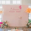Fairy 1st birthday party setup with pastel panel backdrop, giant flowers, florals, mushrooms, and custom fairy signage.