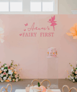 Fairy 1st birthday party setup with pastel panel backdrop, giant flowers, florals, mushrooms, and custom fairy signage.