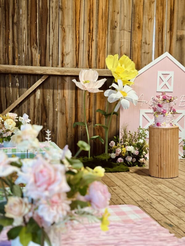 A farm-themed celebration at Earthbound Kids with pink farmhouse backdrop, oversized handmade flowers, cake stand and personalized signage at Earthbound Kids Uxbridge.