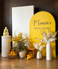 Lemon Blossom Package featuring a yellow arch backdrop with custom bridal shower lettering, white panel, lemon baskets, white vases, yellow florals, greenery, and a cake plinth.