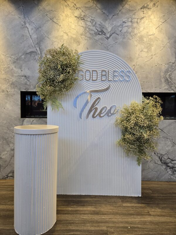 Custom-colored white ripple backdrop with silver "God Bless Theo" script and baby's breath floral accents for a baptism party at Chateau Le Parc in Vaughan.
