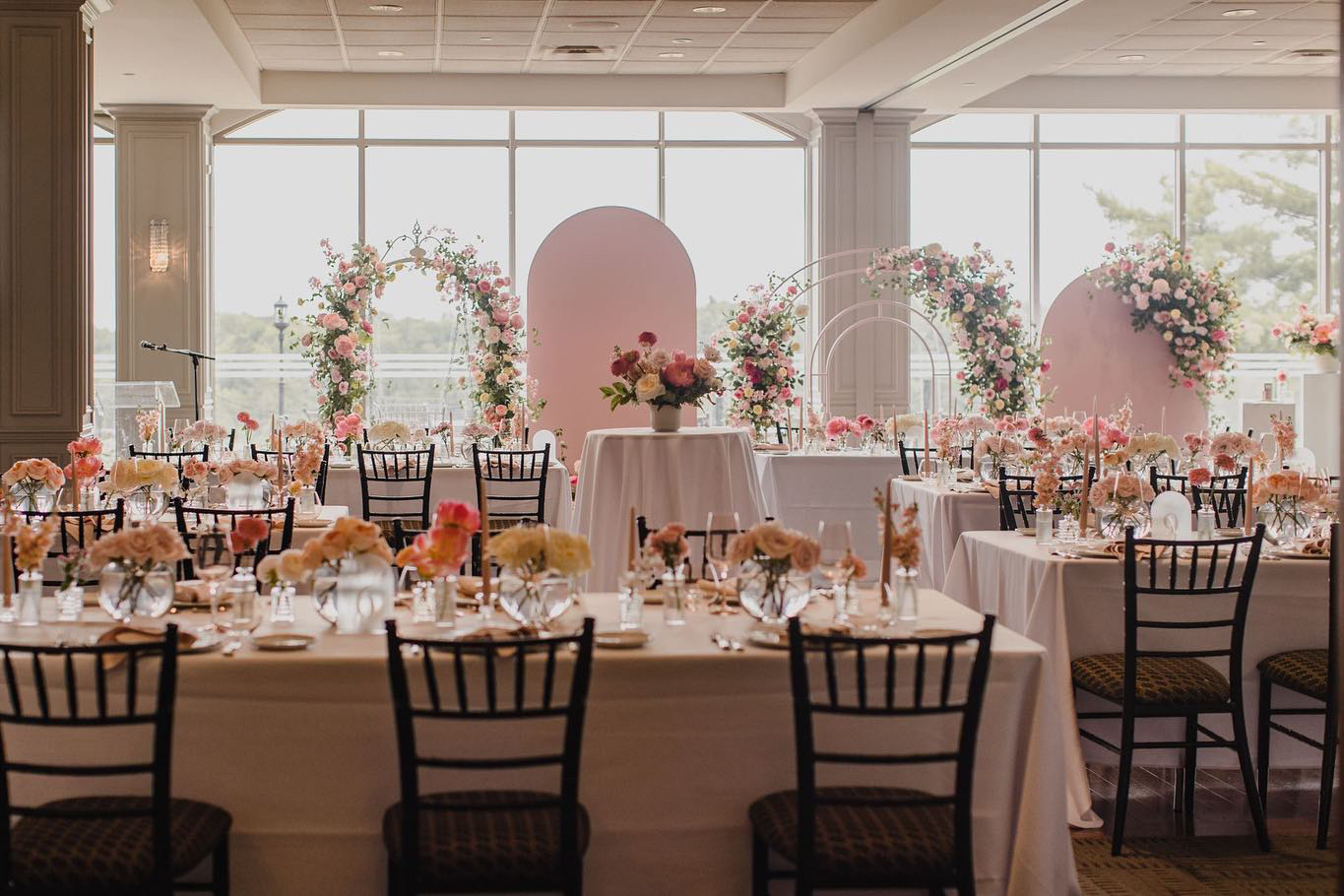 Blush pink arched backdrops and floral installations set up behind dining tables for a reception at Copper Creek Golf Club in Kleinburg, Vaughan.