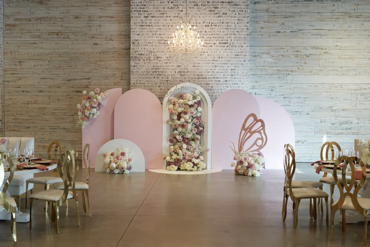 Multi-layered pale pink and rose arch backdrop featuring lush floral arrangements and a large floral cascade, a standing butterfly prop, and a crystal chandelier, styled for a kid's birthday party at W Event Boutique in Woodbridge, Vaughan.