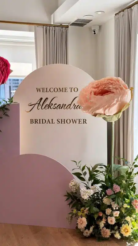 A pink and white arched backdrop with oversized paper peonies and a personalized gold decal for a bridal shower at Sassafraz restaurant.
