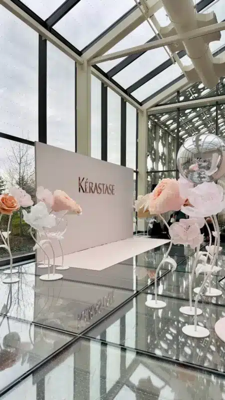 A blush pink Kérastase photo backdrop on a glass floor, surrounded by our giant flower rentals in Toronto featuring pastel silk roses and peonies.