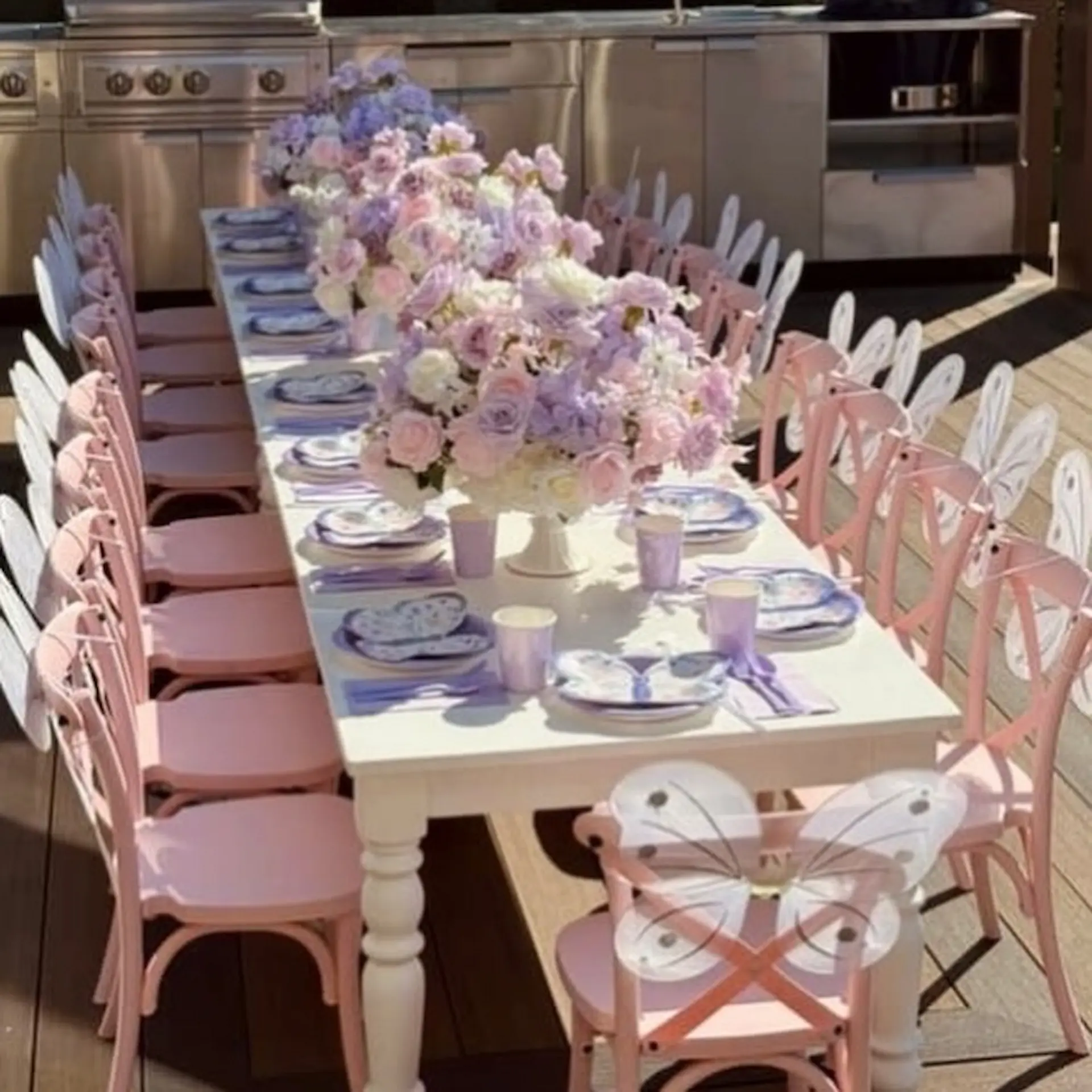 Fairy butterfly kids table setup with pink chairs, white butterfly wings, pastel floral centrepieces, and lavender place settings.
