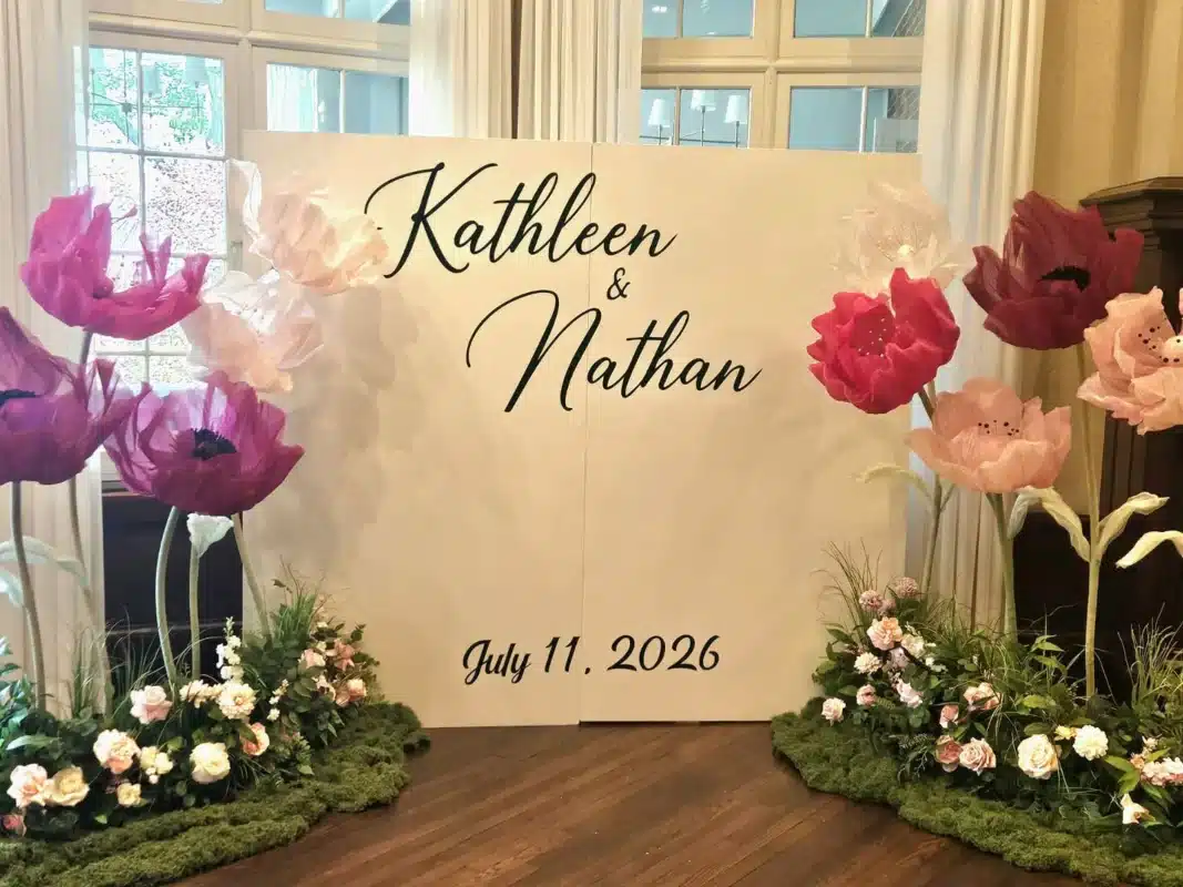 Custom wedding backdrop rental with oversized fuchsia, pink, and oversized paper flowers on moss bases, featuring the names Kathleen and Nathan and the date July 11, 2026, at Scarboro Golf Club.