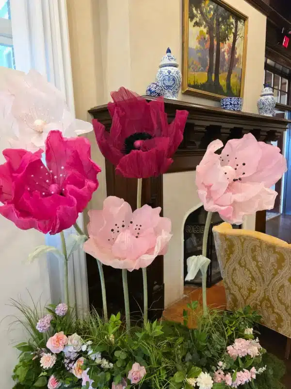 It clearly describes the image for accessibility and search engines while naturally embedding long-tail search terms like "giant standing paper poppy flower rentals" without keyword stuffing.
