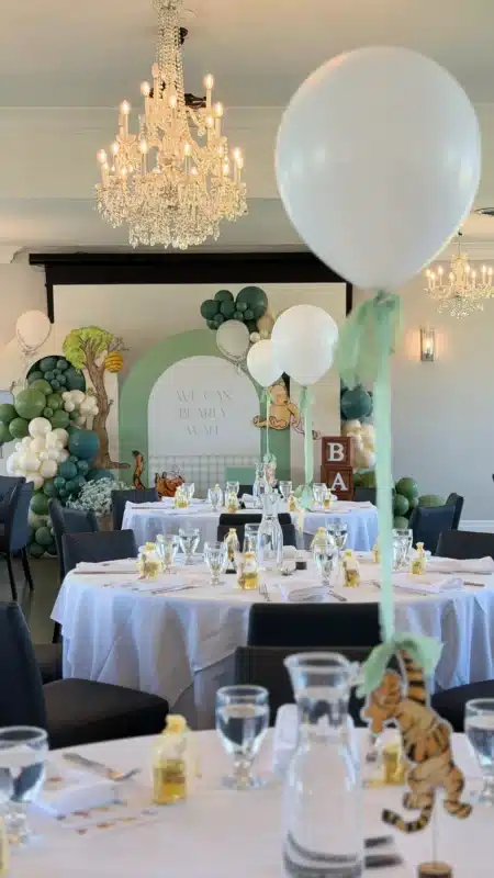 A Winnie the Pooh themed baby shower setup at Cardinal Golf Club in Richmond Hill, featuring a "We Can Bearly Wait" backdrop, green and white balloon garlands, and round tables with honey jar party favors.