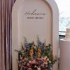 Blushing Garden Arch backdrop with custom bridal brunch lettering and a lush floral arrangement in blush pink, ivory, dusty blue, peach, and greenery.