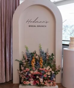 Blushing Garden Arch backdrop with custom bridal brunch lettering and a lush floral arrangement in blush pink, ivory, dusty blue, peach, and greenery.
