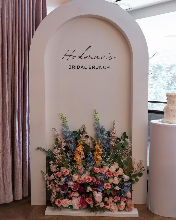 Blushing Garden Arch backdrop with custom bridal brunch lettering and a lush floral arrangement in blush pink, ivory, dusty blue, peach, and greenery.