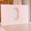 Elegant Signature Backdrop with two plain square side panels and a decorative oval floral centre panel, set in a modern indoor venue with light wood flooring and tall architectural walls.