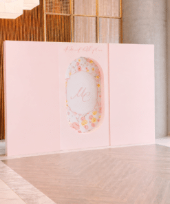 Elegant Signature Backdrop with two plain square side panels and a decorative oval floral centre panel, set in a modern indoor venue with light wood flooring and tall architectural walls.