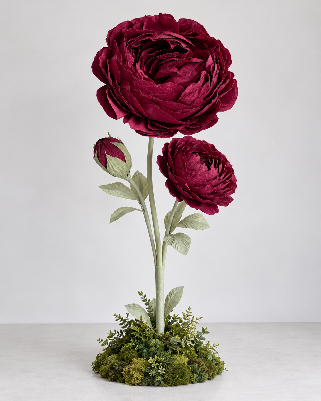 burgundy peony flower trio with two open blooms and one bud on tall green stems, finished with leaves and a lush moss-covered botanical base.