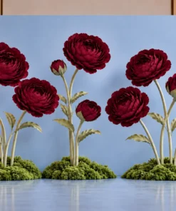 Giant burgundy peony flowers with coordinating buds, tall sculptural stems, and green moss-covered bases displayed in front of a light blue event backdrop.