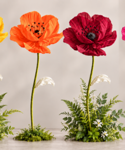 giant silk poppy flowers in yellow, orange, deep burgundy red, and fuchsia pink with tall green stems and decorative leaves.